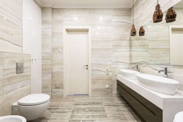 A bathroom with travertine-look tile on the walls and floor, a floating vanity and a wall-hung toilet.