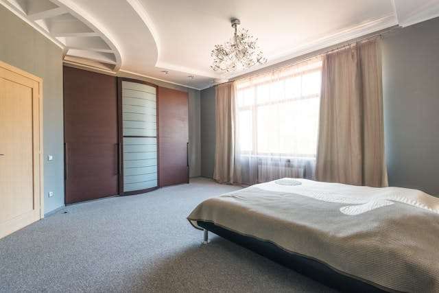 A bedroom with grey carpet, a low bed and a large wardrobe.