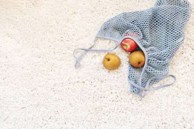 A mesh bag of apples and pears on a plush cream carpet.