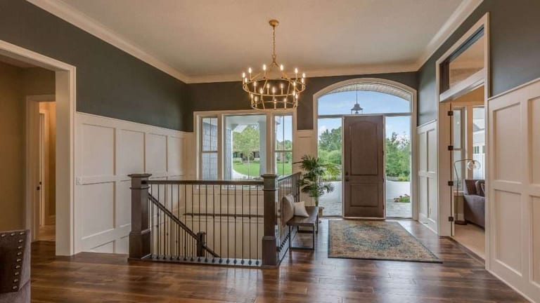 An entry hall with dark hardwood flooring, a chandelier, panelled walls and a stair railing.