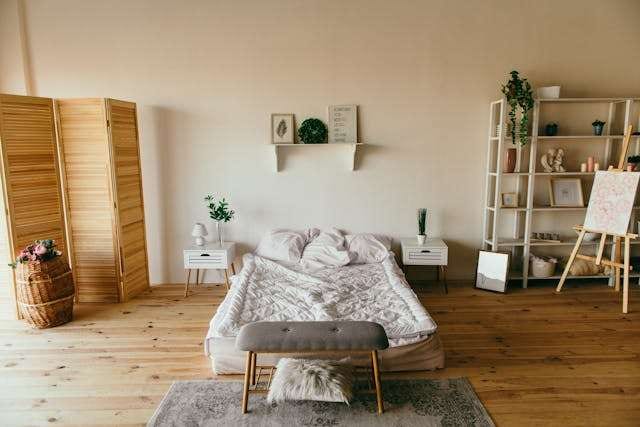 A bedroom with a warm pine plank floor, a low bed and white shelving.