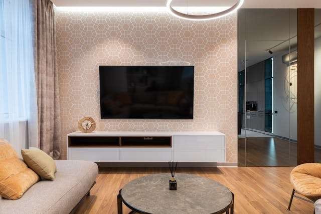 A living room with a light wood floor, a round stone coffee table and a patterned feature wall.