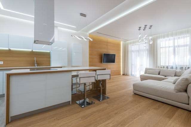 An open-plan kitchen and living room with a light oak floor, white island and grey sofa.