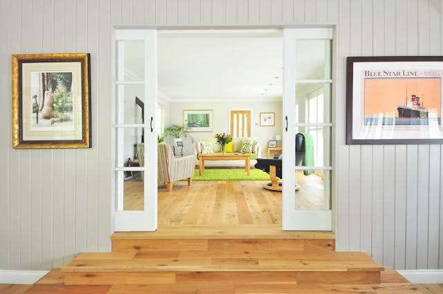 A raised entry step in light wood flooring leading through glass French doors into a sunny living room.