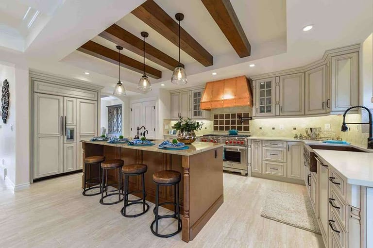 Luxury Infills: a kitchen with a copper range hood, cream cabinetry, a dark-stained wood island with leather stools and a pale large-format tile floor.