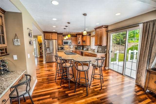 A kitchen with glossy multi-toned hardwood flooring, wood cabinets and a granite island with stools.
