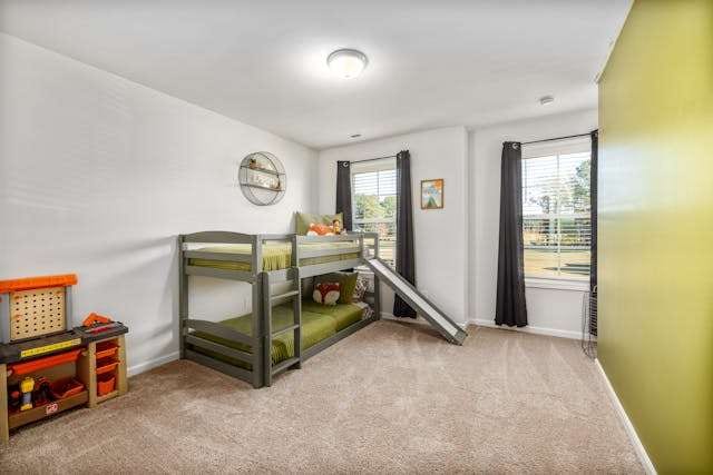 A child's bedroom with beige carpet, a bunk bed with a slide and a green accent wall.