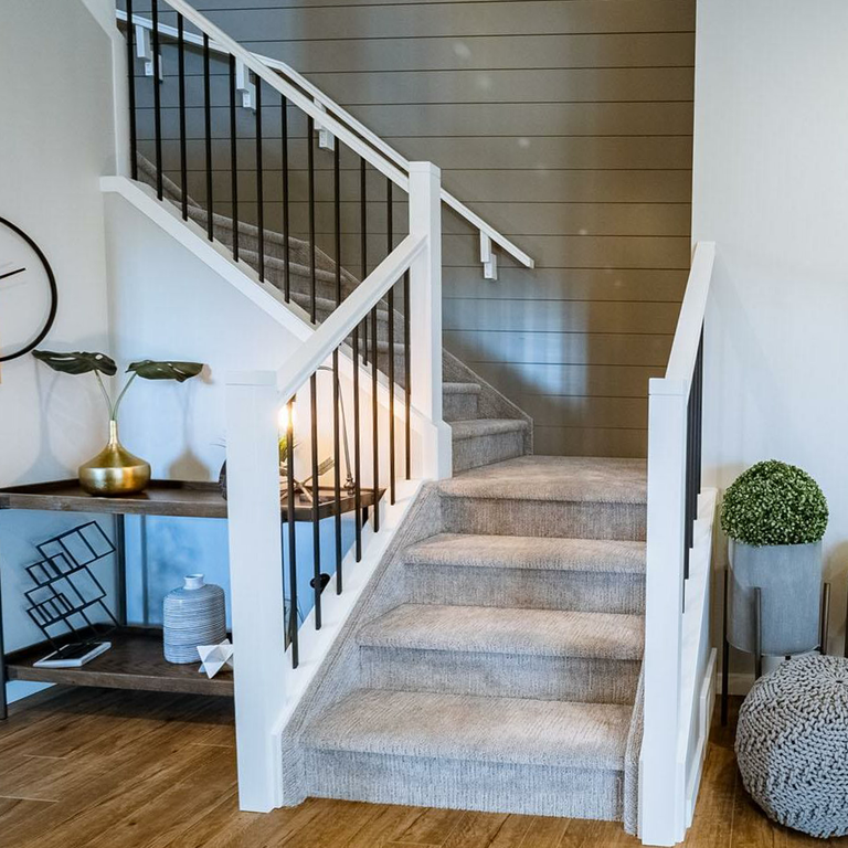 A staircase with grey carpet on the treads and white painted risers and stringers, above a wood-plank floor.