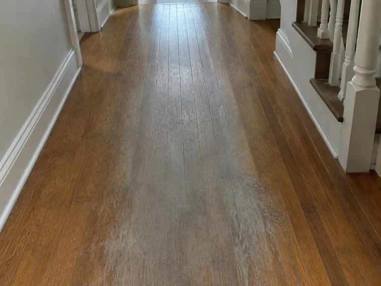 A hallway hardwood floor with the finish worn through to bare wood along the main walking path.