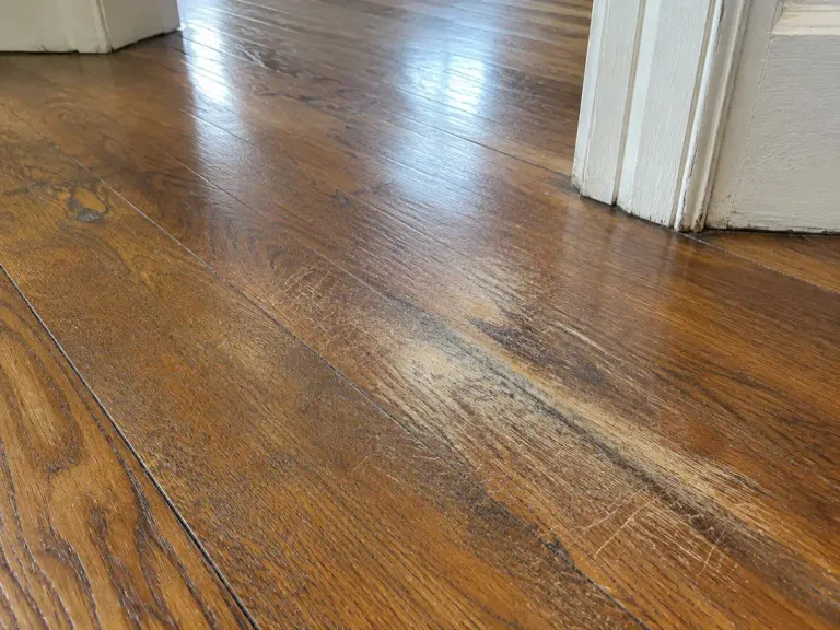 An older oak hardwood floor with deep scratches and a worn path through the finish near a doorway.