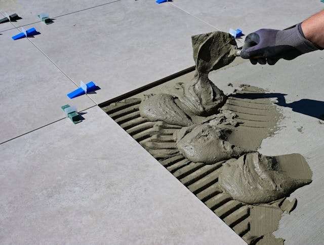 A gloved hand spreading thinset mortar with a trowel to set large-format tile.