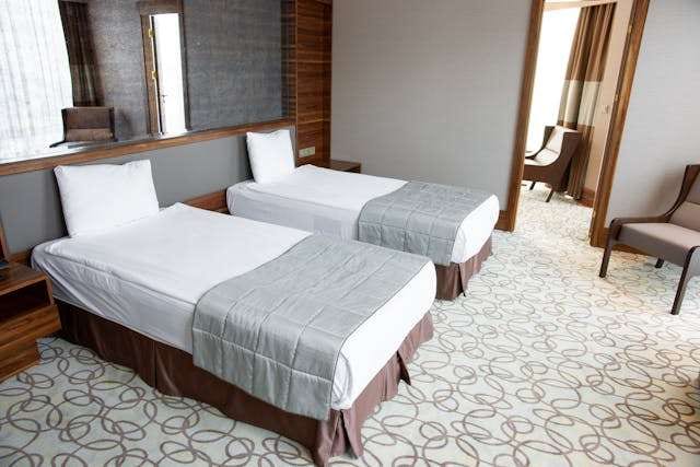 A twin hotel room with a swirl-patterned carpet and two white beds.