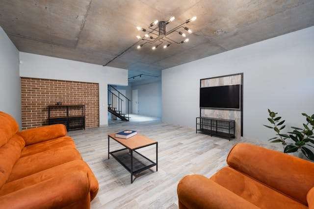 A loft living room with grey wood-look plank flooring, orange sofas and a brick fireplace.