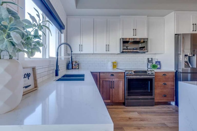 A white quartz counter running the length of a kitchen with white upper cabinets, dark-stained wood lower cabinets and a light plank floor.