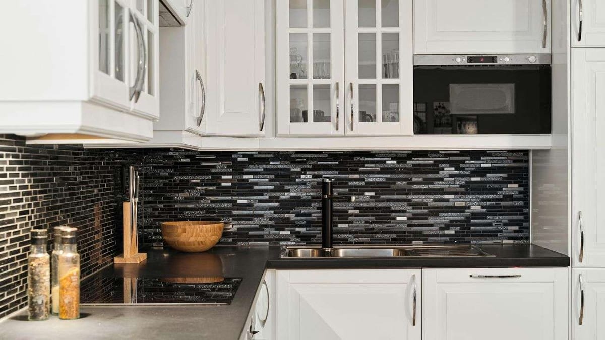 White kitchen cabinets with a black and grey glass mosaic tile backsplash.