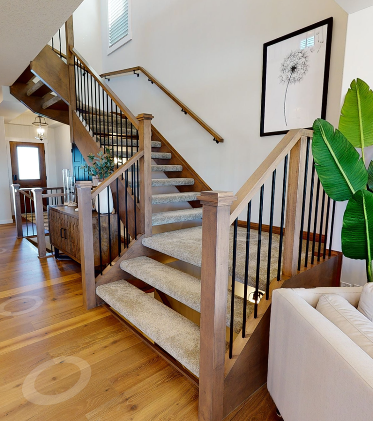 An oak-railed staircase with a carpeted runner over the treads, rising from a light wood-plank entryway.
