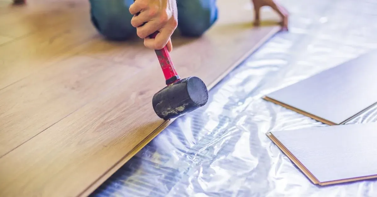 A rubber mallet tapping a laminate plank into place over a foil-backed underlay.
