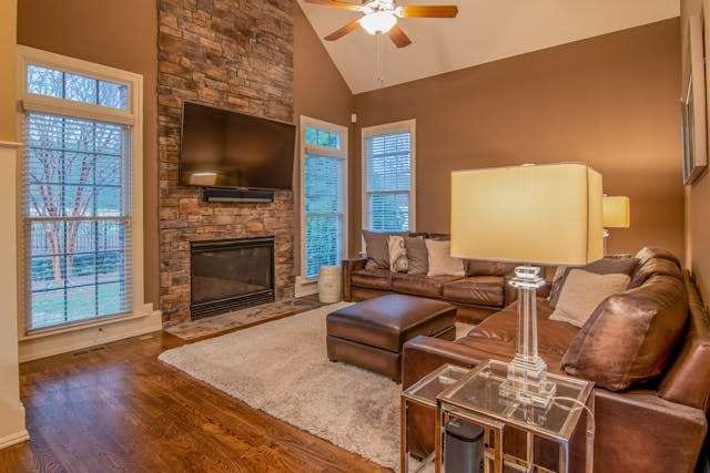 A family room with a dark hardwood floor, a brown leather sofa and a stone fireplace.