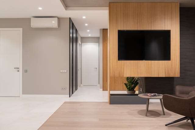 A modern living space with a light wood-look floor, a wood-panelled TV wall and grey walls.