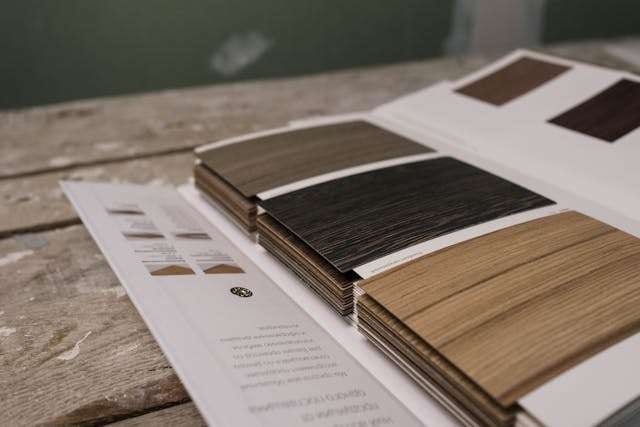 Wood-look flooring samples in grey, black and oak tones fanned on a swatch card.