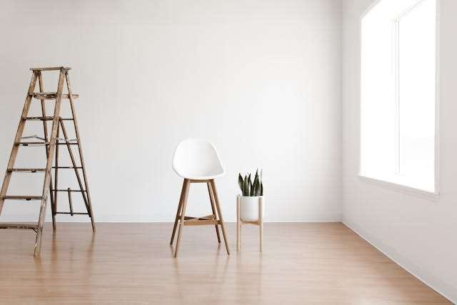 An empty white room with a light wood floor, a stepladder and a white stool.