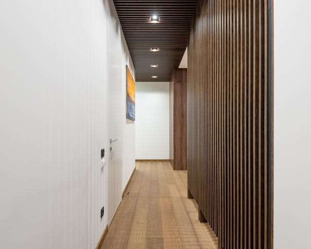 A narrow hallway with a light wood plank floor and a dark wood slat wall.