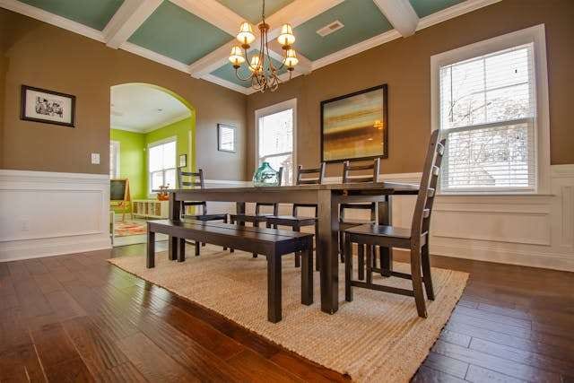 A dining room with a dark hand-scraped hardwood floor, a long table and a coffered ceiling.