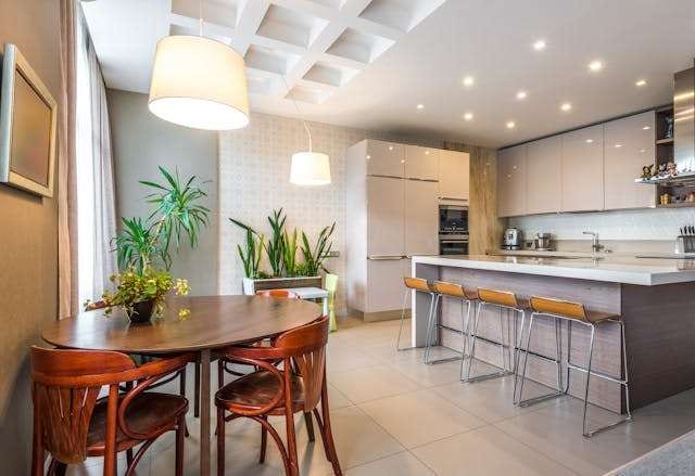 A kitchen and dining area with large pale floor tile, a wooden table and a grey island with stools.