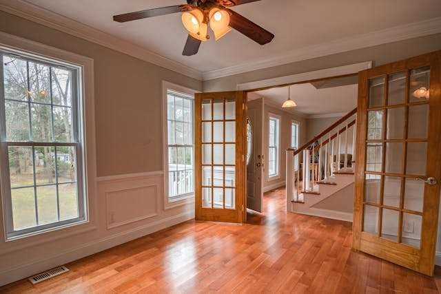 An empty room with a glossy reddish hardwood floor and glazed French doors to the hall.