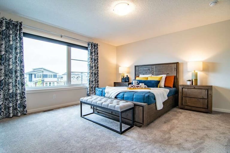 A bedroom with grey carpet, a dark upholstered bed and patterned curtains.