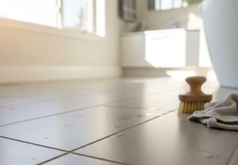 A scrub brush and cloth on a white tile floor with grey grout lines.