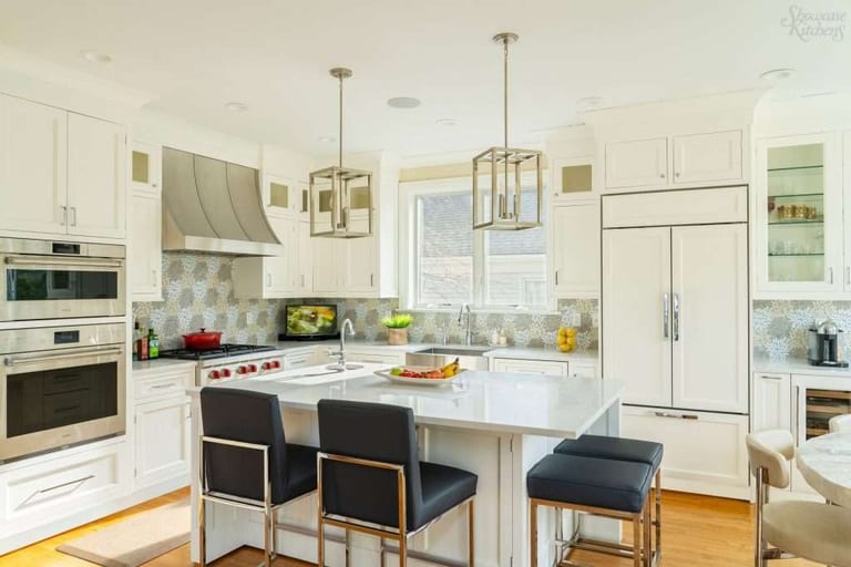 Light hardwood flooring in a white kitchen with a large island, lantern pendants and bar stools.