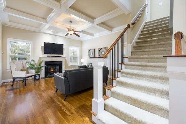 A family room with a medium hardwood floor and a carpeted staircase with white risers.