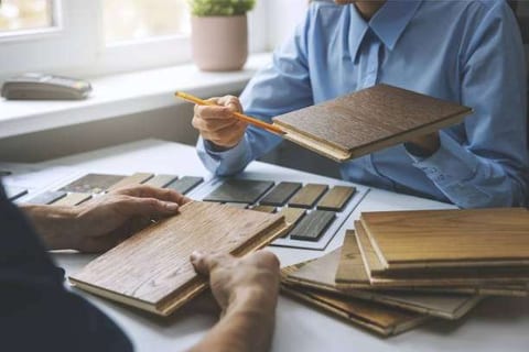 Two people at a table comparing wood flooring sample boards laid out in a fan of stains and tones.