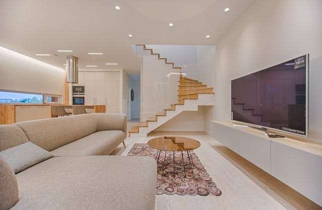 An open-plan living room with a pale floor, a beige sofa and a wood-tread staircase.