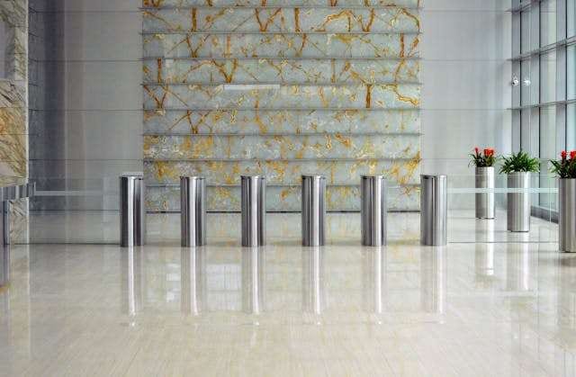An office lobby with a polished white tile floor, entry turnstiles and a stone feature wall.