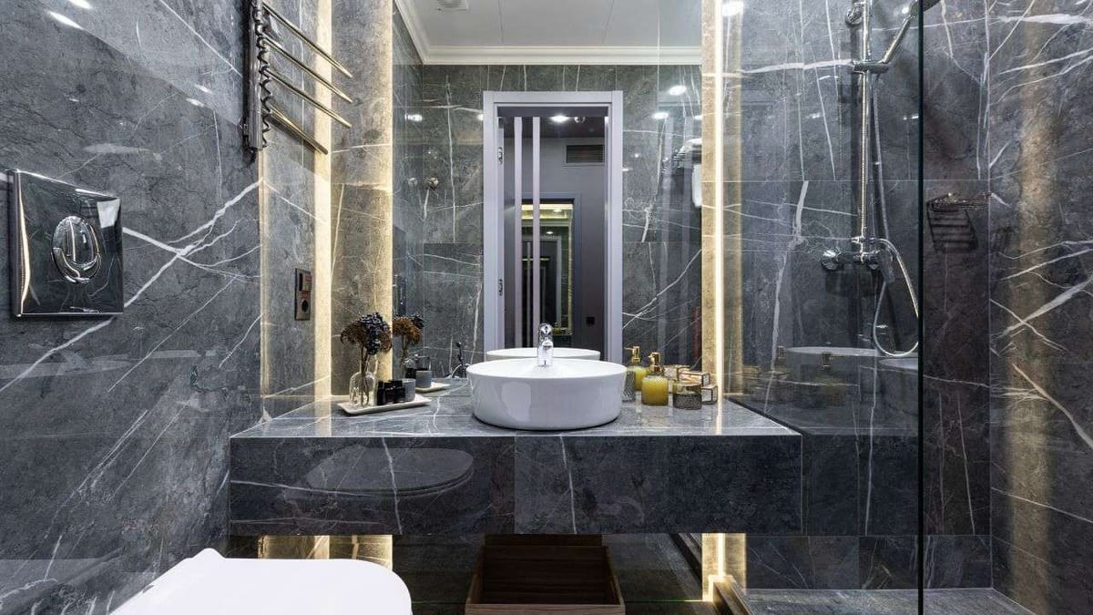 A bathroom with dark grey marble-look tile, a vessel sink and a glass shower.