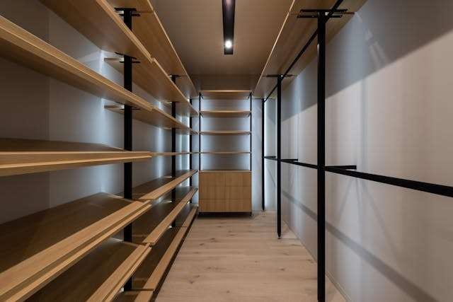 A walk-in closet with open wooden shelving and a light wood floor.
