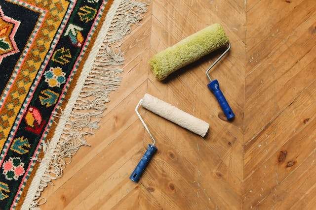 Paint rollers lying on a herringbone wood floor beside a colourful rug.