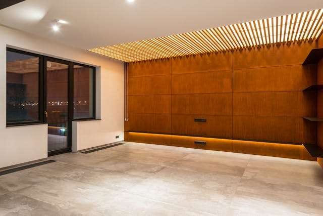 An empty room with pale stone-look large-format tile and a copper-toned panelled wall.