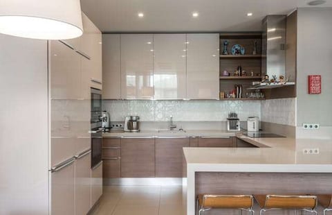A glossy cream kitchen with an L-shaped counter and pale large-format floor tile.