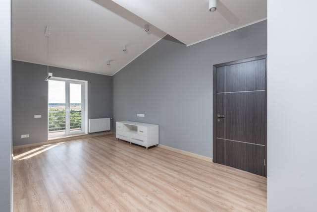 An empty room with light oak-look laminate flooring and grey walls.