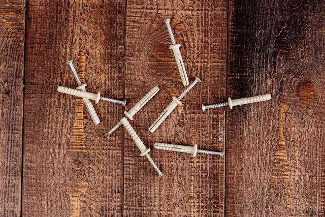 Plastic wall anchors and screws scattered on a rough dark wood surface.