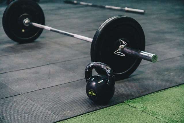 A barbell and kettlebell on black rubber gym flooring.