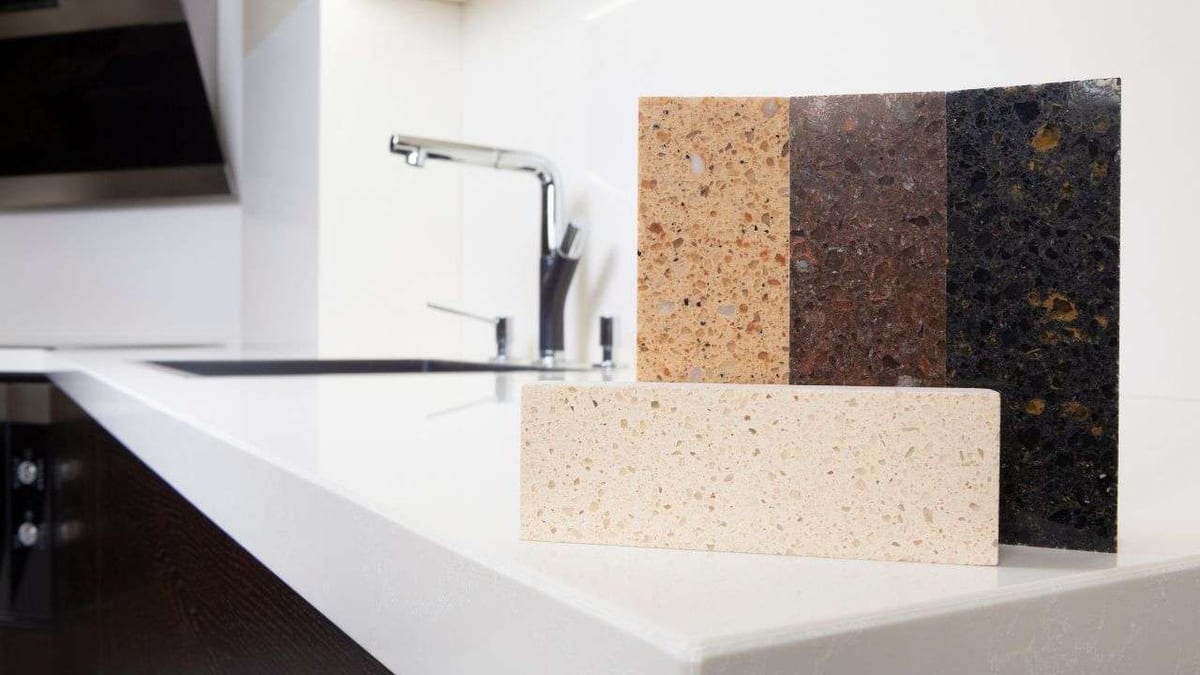 Quartz countertop samples in cream, brown and black on a white kitchen counter.