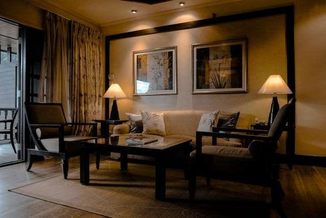 A warmly lit sitting room with a dark wood floor, a cream sofa and dark wood armchairs.