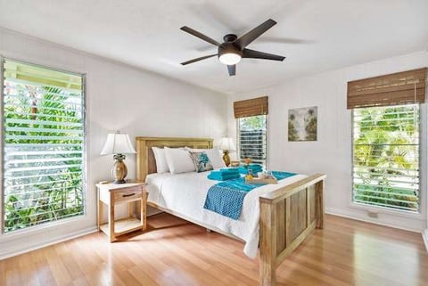 A bright bedroom with a glossy light hardwood floor, a wooden bed and a ceiling fan.