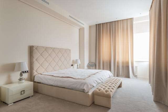A bedroom with plush beige carpet, a tufted headboard and an upholstered bench.