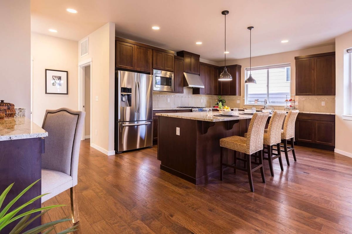 A kitchen with dark cabinets, a granite island and a medium-brown hardwood floor.