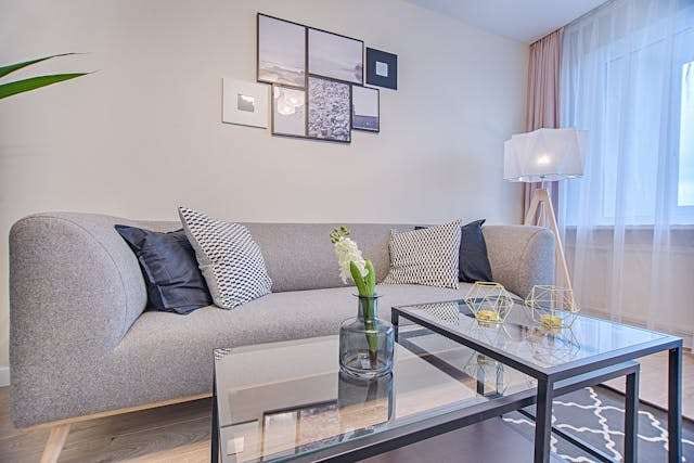 A living room with a grey sofa, a glass coffee table and patterned cushions.